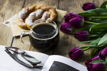 Still life with tulips, a book, coffee and a pretzel on the old wooden background