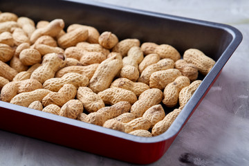 Unpeeled raw peanut on baking tray over white textured background, selective focus, shallow depth of field.