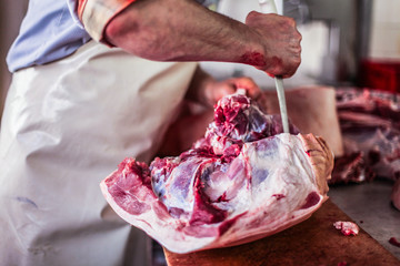 butcher cut raw meat with a knife at table in the slaughterhouse