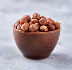 Hazelnuts in wooden bowl on wihite background with copy space, top view, selective focus.