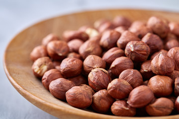 Hazelnuts in wooden bowl on wihite background with copy space, top view, selective focus.