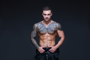 The man with a muscular naked torso with tattoos on the dark background. ABS