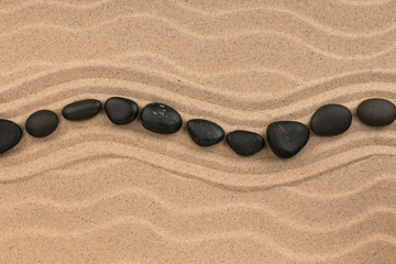 Fototapeta na wymiar Line made of black stones lying wavy, on sand dune.