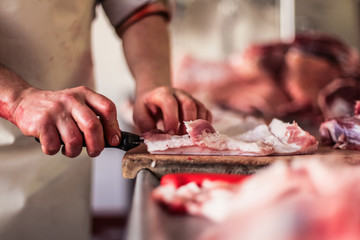 butcher cut raw meat of a pig with a knife at table in the slaughterhouse