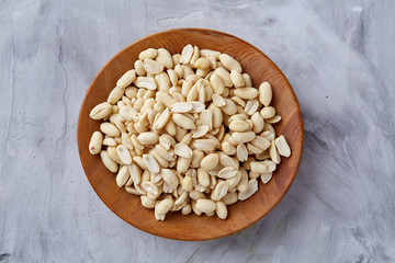 Peanuts in wooden plate isolated over white textured background, top view, close-up.