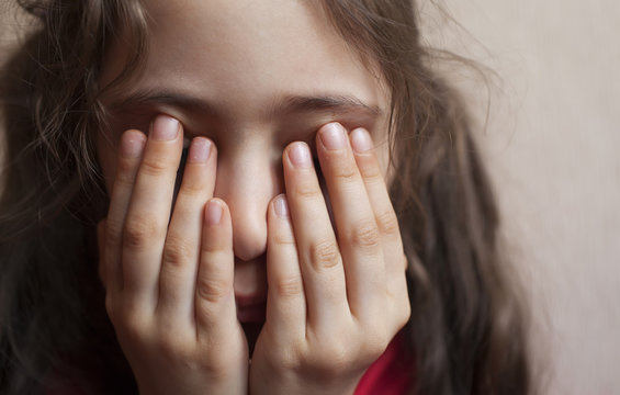 Portrait of a little girl of six years closes her eyes with her hands