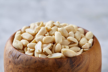 Peanuts in wooden plate isolated over white textured background, top view, close-up.
