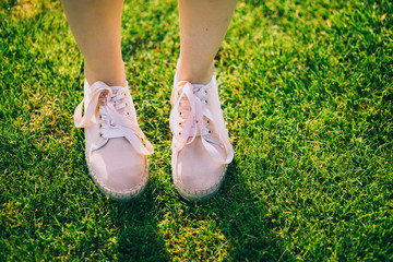 Pink sneakers on woman's legs on grass during sunny summer day