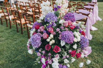 flower arrangement stands in the wedding ceremony area on the background of chairs decorated with fabric and flowers