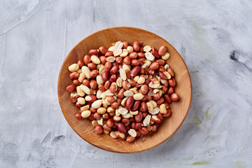 Raw mixed peanuts in wooden plate isolated over white textured background, top view, close-up.