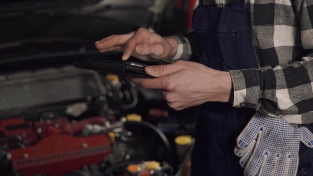 Close up footage in slow motion of auto service technician using digital tablet to examine the vehicle issues. Car repair, maintenance, people concept.