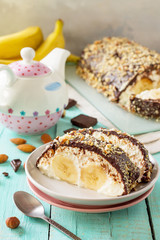 Homemade dessert with cream cheese, banana, chocolate icing and nuts on a rustic wooden table.