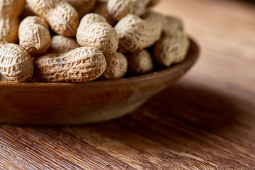 Unpeeled peanuts in wooden bowl over rustic wooden background closeup, selective focus