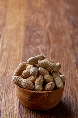 Unpeeled peanuts in wooden bowl over rustic wooden background closeup, selective focus