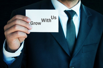 Businessman showing Grow With Us text on business card.