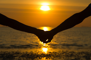 Close up on silhouette of couple's arms holding hands at sunset by the sea to celebrate Valentines...