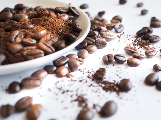 brown coffee beans and ground coffee on a white cup.