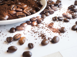 brown coffee beans and ground coffee on a white cup.