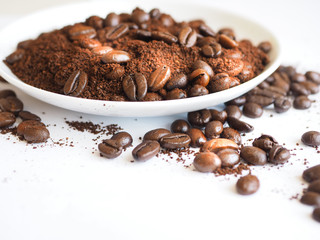 brown coffee beans and ground coffee on a white cup.