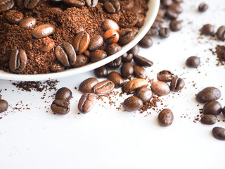 brown coffee beans and ground coffee on a white cup.
