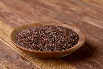 Flax seeds in a plate on wooden background, top view, close-up.