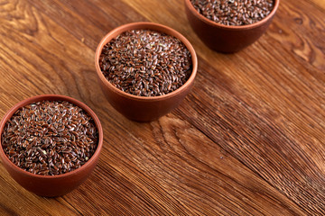 Three ceramic bowls with flaxseeds arrenged in row over wooden background, top view, selective focus