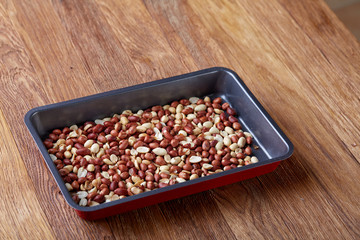 Mix of peeled raw peanut on baking tray over wooden background, selective focus, shallow depth of field.