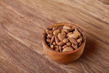 Ceramic bowl of almonds on wooden background, top view, close-up, selective focus.