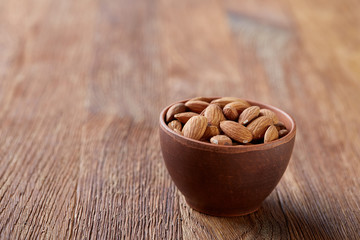 Ceramic bowl of almonds on wooden background, top view, close-up, selective focus.