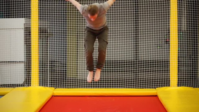 Confident athletic young man training his stunts on a trampoline. He does flip and fall on the back.