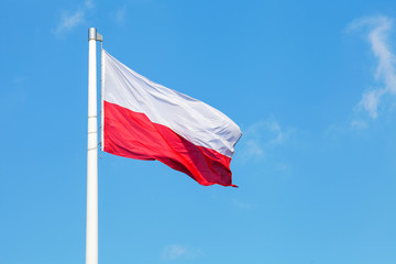 Naklejka na ściany i meble Polish national flag waving on the wind against blue cloudy sky