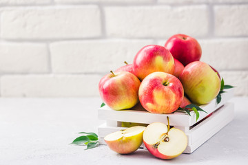 Ripe fresh red apples in white wooden box on light background. Selective focus, space for text.