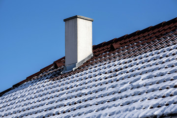 white chimney on a red roof covered with snow in winter