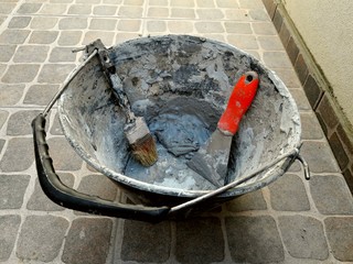 Espátula, pincel y balde de construcción usados y gastados sobre piso adoquín