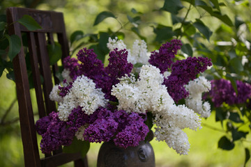 A bouquet of lilac in a vase on a chair in the garden, fragment, close-up, soft focus.