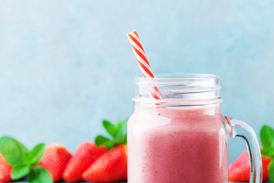 Pink strawberry smoothie or milkshake in mason jar on turquoise table. Healthy food for breakfast and snack.