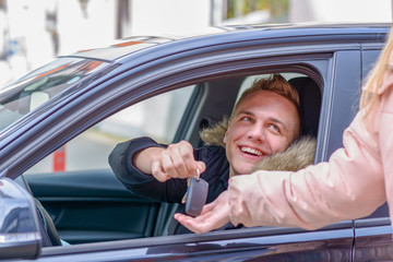 Smiling young man in a car handing over his keys
