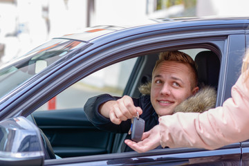 Smiling young man in a car handing over his keys