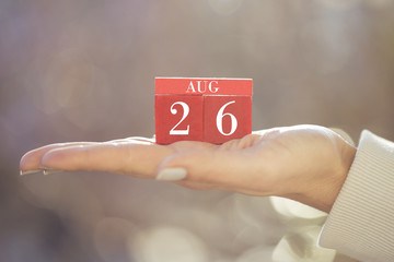 the woman is holding a red wooden calendar. Red wooden cube shape calendar for AUG 26 with hand 