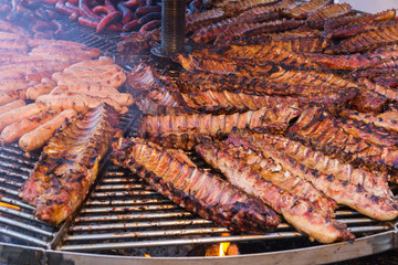 Gran parrillada de carne asada encendida y con humo en feria  al aire libre. Costillas y carne de cerdo, ternera, cordero,  chorizos y salchichas