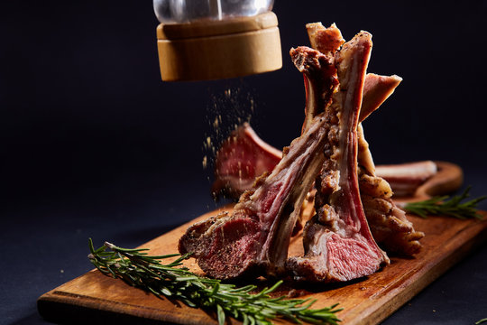 Rack of lamb with rosemary on wooden cutting board over dark background, side view, selective focus