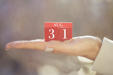 the woman is holding a red wooden calendar. Red wooden cube shape calendar for AUG 31 with hand 