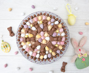 Obraz na płótnie Canvas Looking down from above onto an Easter celebration cake decorated with mini easter eggs and chocolate bunnies on a white background with easter decorations