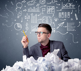 Young businessman sitting behind crumpled paper with mixed drawings over his head