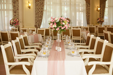 Beautiful setting of wedding party in restaurant. Tables and chairs decorated with flowers and fabrics gently pink in color