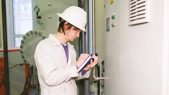 The white helmet engineer records the readings from the display of the electric control Cabinet and gas equipment sensors.