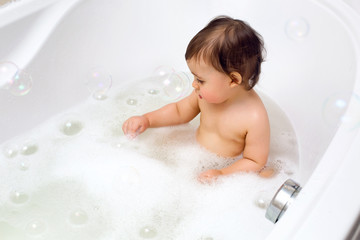 baby boy sitting in bath with water and foam