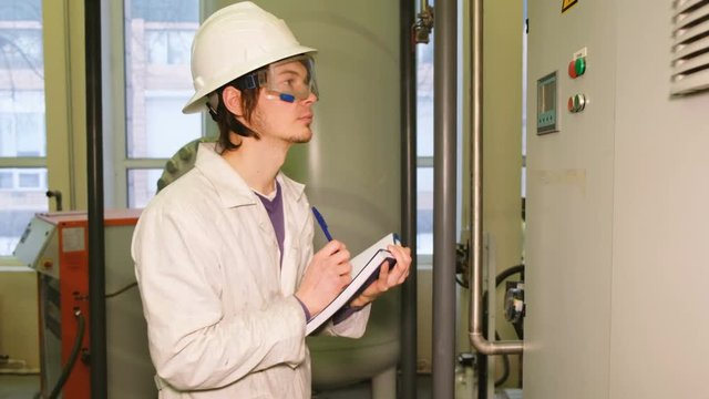 The inspector in safety glasses, helmet and robe takes readings from gas installations, records the readings of the pressure gauge and sensors.