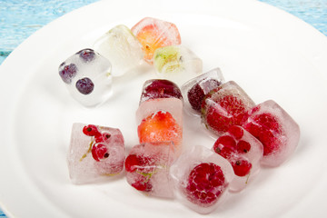 Berries frozen in ice cubes with mint on plate.