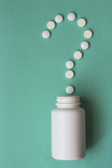 A question mark, laid out of pills and a white plastic bottle on a blue background. Medical concept